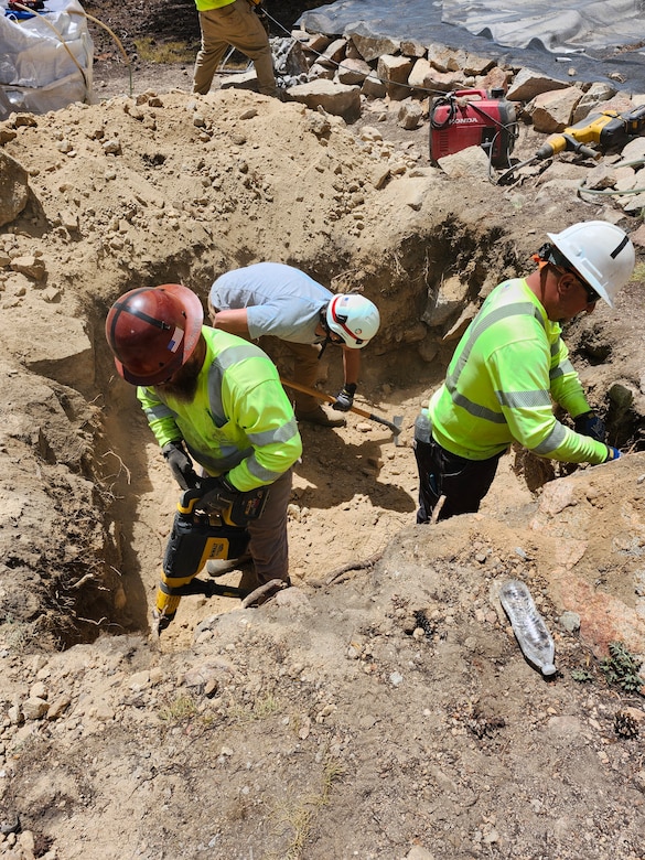 Three men digging in ditch.