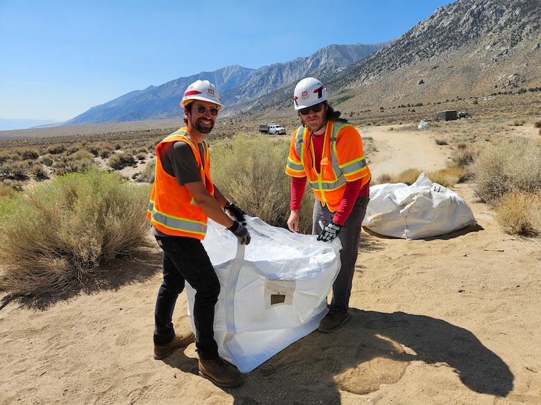 Two men holding bag of concrete.