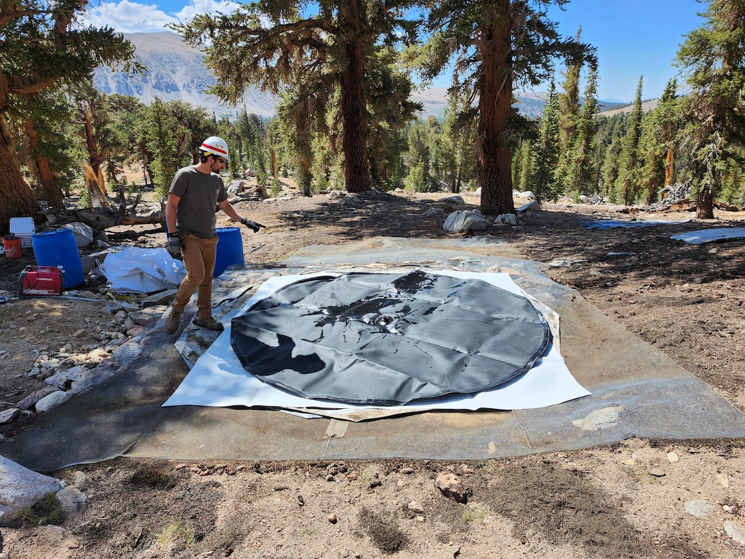 Man points to snow pillow laid out on the ground in the forest.