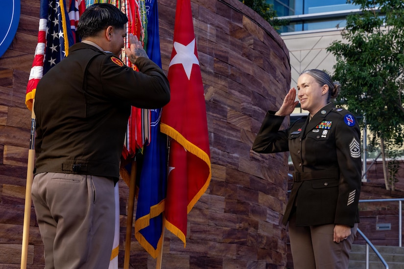 U.S. Army Sgt. Maj. Krystal Chambers (right) of U.S. Army Pacific, takes the honor of being the first noncommissioned officer (NCO) to salute her husband, U.S. Army Capt. Jeremy Chambers (left), and to receive the silver dollar coin, Dec. 4, 2025, Fort Shafter, Hawaii.