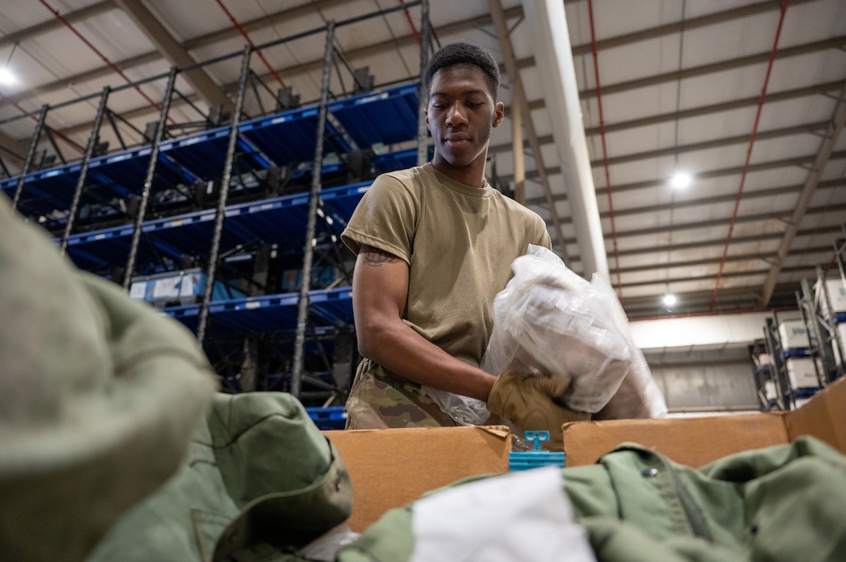 An Airman in a warehouse places items into a cardboard bin filled with A-Bags