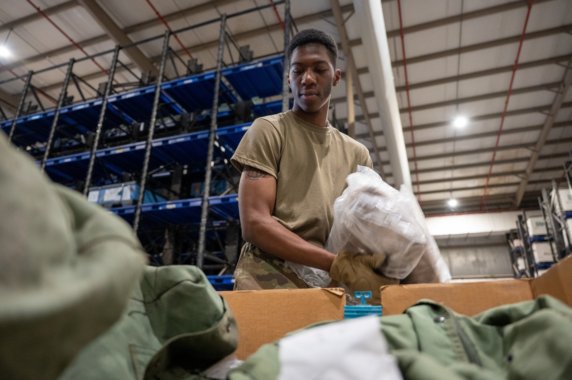 An Airman in a warehouse places items into a cardboard bin filled with A-Bags