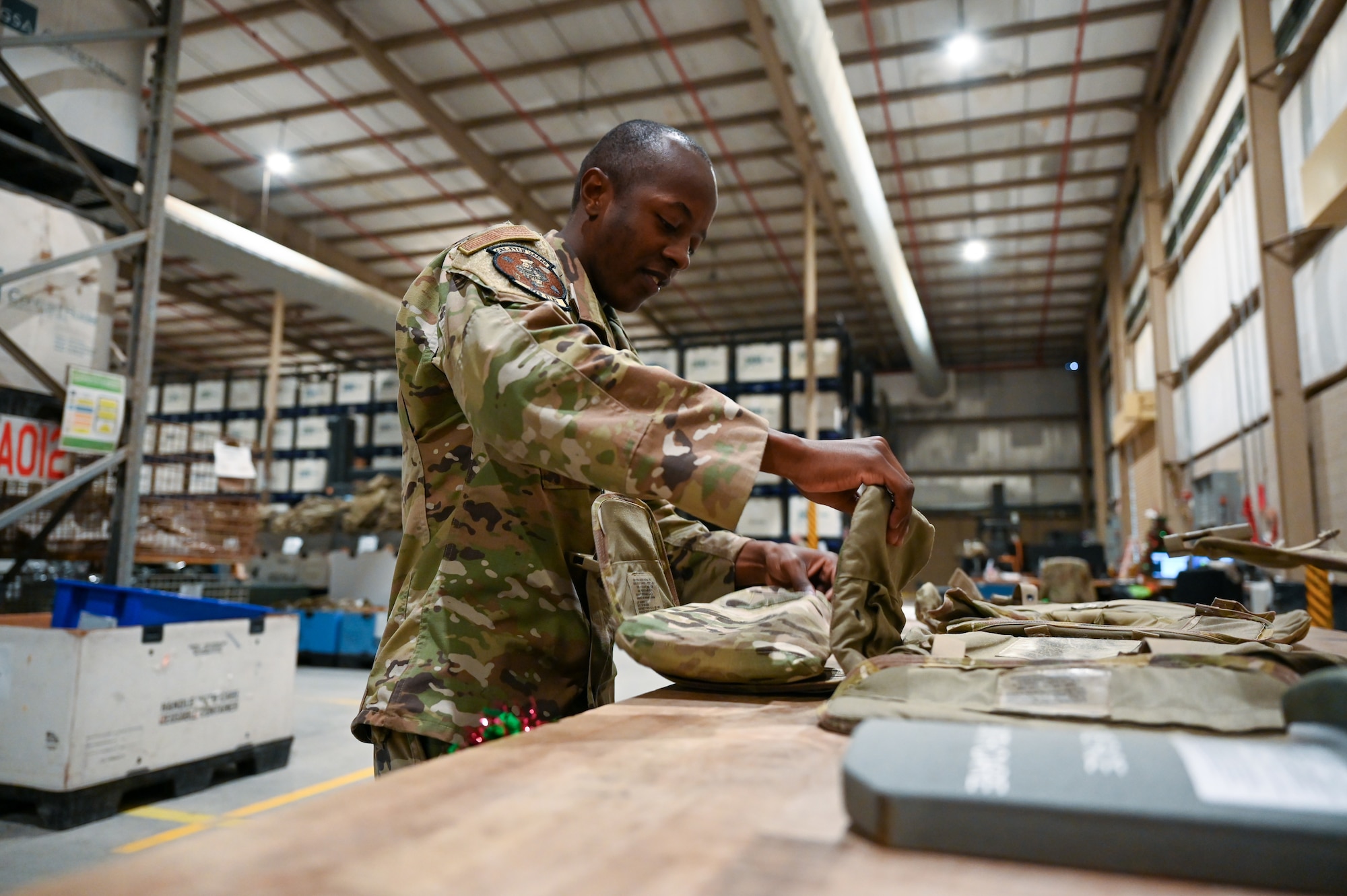 An Airman in a warehouse opens flaps of a tactical vest lying on a table