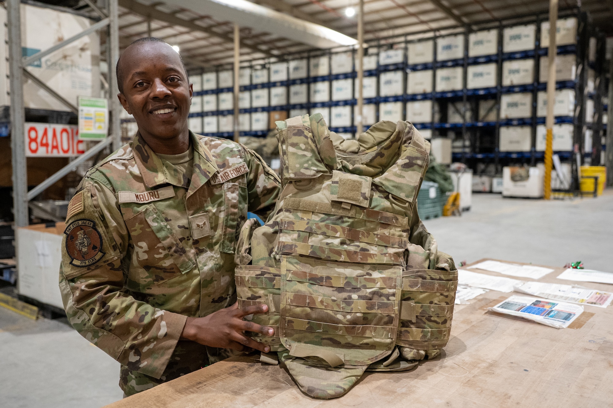 An Airman in a warehouse holds up a tactical vest on a table