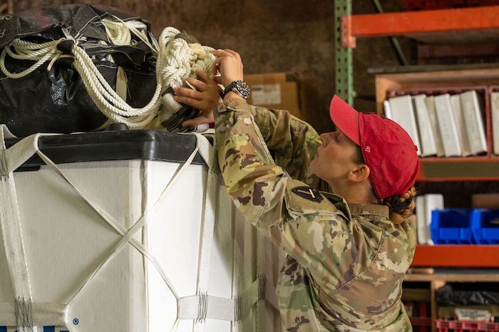 A Soldier wearing a red rigger cap lifts and inspects paracord on top of a container delivery system