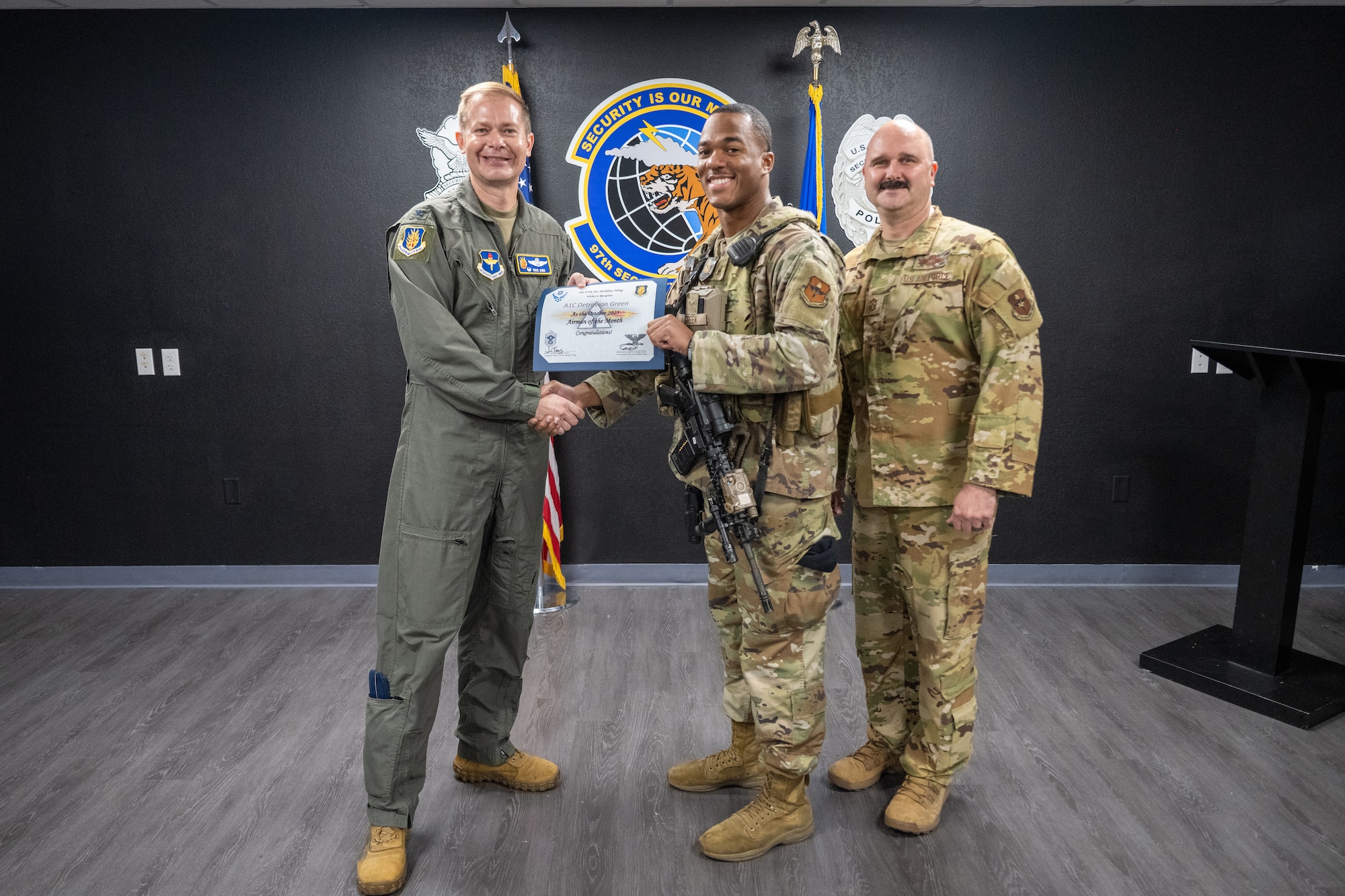 U.S. Air Force Col. Richard Kind, left, 97th Air Mobility Wing (AMW) commander , and Chief Master Sgt. Jonny Adams, right, 97th AMW command chief , hands an award to Airman 1st Class Detravion Green, 97th Security Forces logistics supply technician at Altus Air Force Base, Oklahoma, Nov. 20, 2025. Green was named the Airman of the Month for October 2025 (U.S. Air Force Photo by Airman 1st Class Nathan Langston)