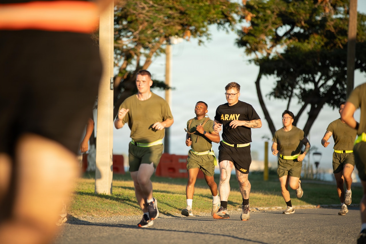 A group of people in athletic attire and reflective belts jog on a paved road.