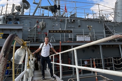 A man stands on the gangway leading up to a ship. He is in civilian cloths.