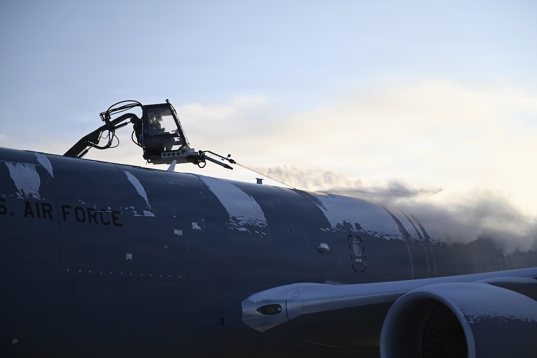 An airman operates a lift to deice a partially visible snowy aircraft.