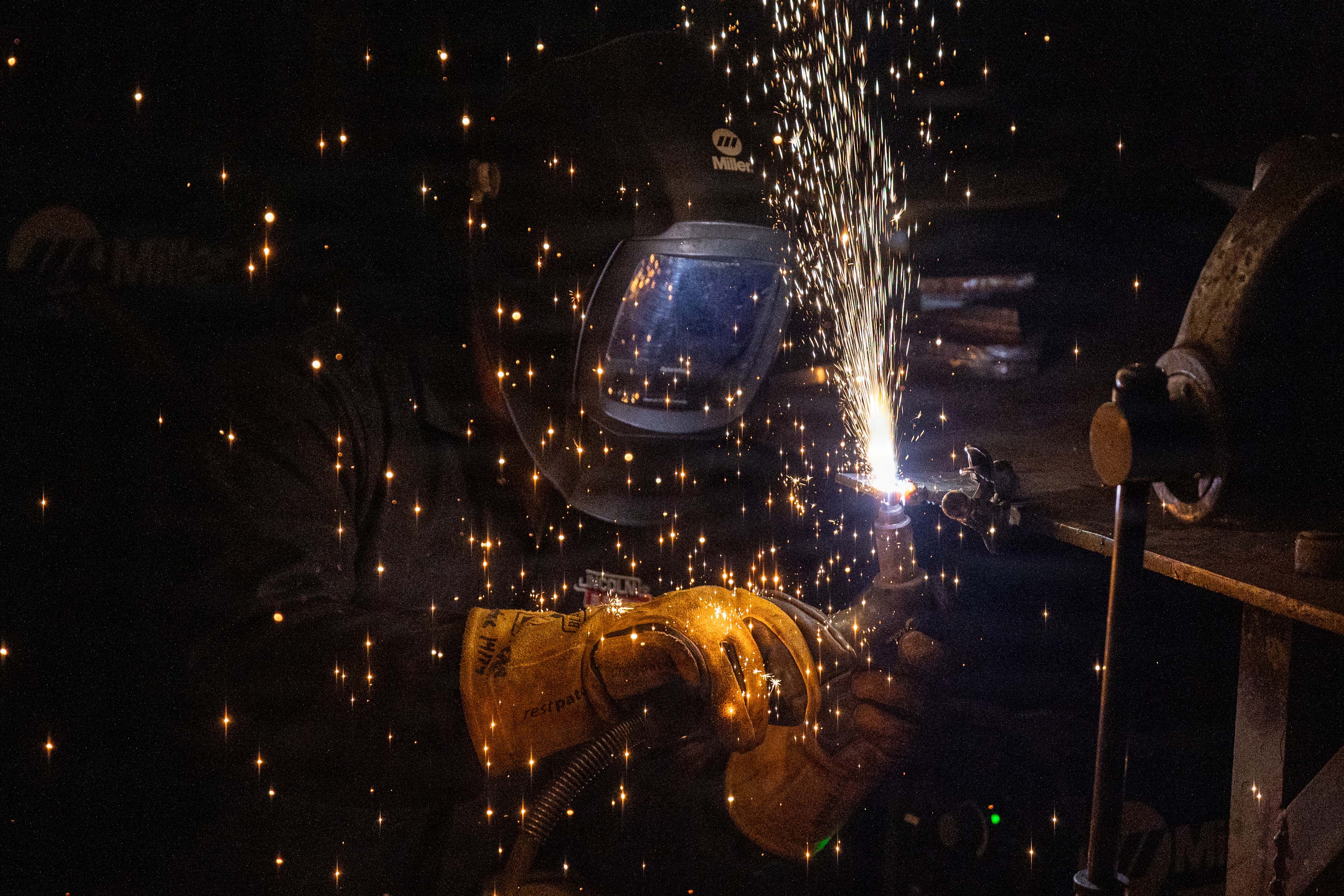 Sparks fly as an airman wearing protective gear cuts into metal in a dark room.