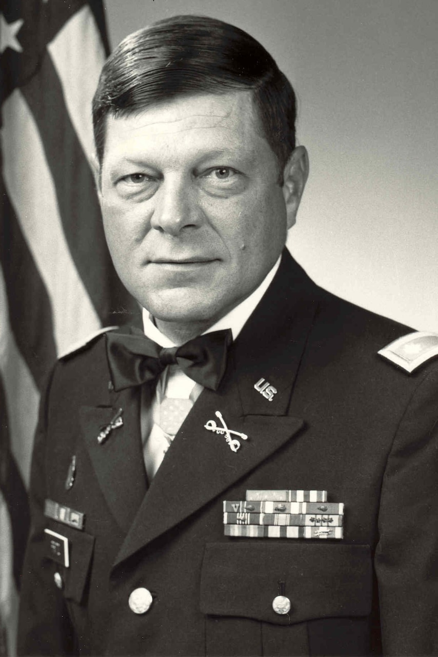 A man wearing a military dress uniform poses for a photo beside an American flag.