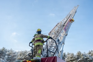 U.S. Air Force Airman 1st Class Jasmin Gonzalez, left, 35th Civil Engineer Squadron fire protection specialist, prepares to climb an aerial ladder with guidance from SrA Bode Hartwig, 35th Civil Engineer Squadron fire protection specialist, at Misawa Air Base, Japan, Jan. 6, 2026. Firefighters serve as a key force protection element, delivering emergency response to safeguard people, aircraft, and mission-critical facilities at Misawa Air Base. (U.S. Air Force photo by Airman 1st Class Adryan Young)