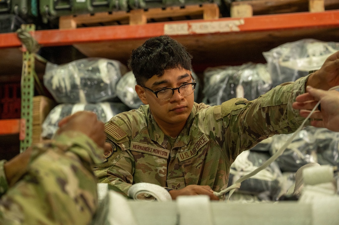 An Airman hands a piece of cord to someone out of frame