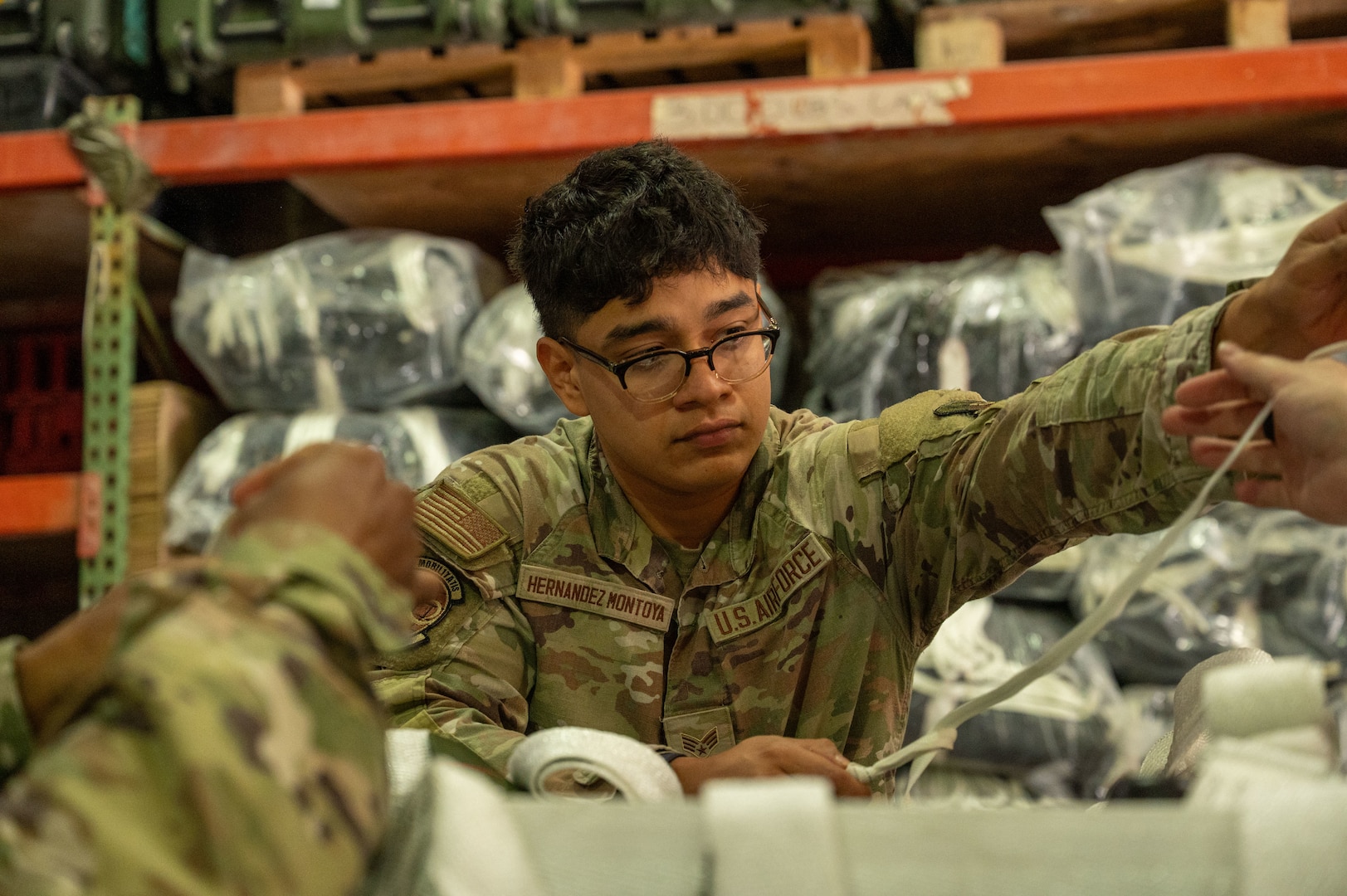 An Airman hands a piece of cord to someone out of frame