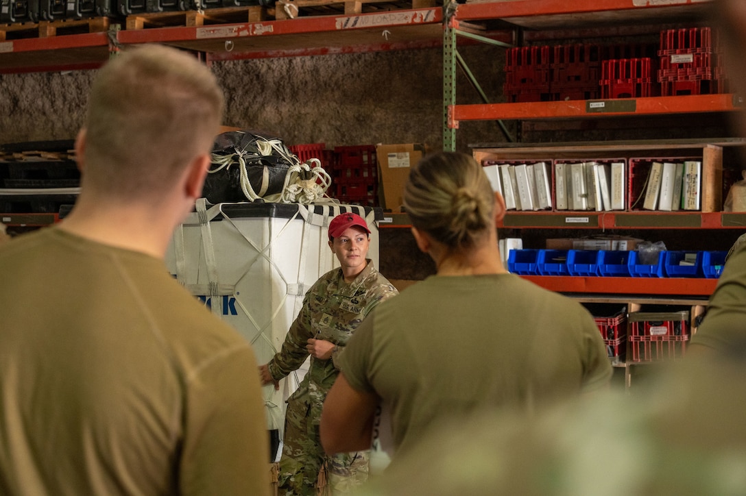 A Soldier gestures toward a container delivery system while Airmen in the foreground look on
