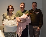Air Force Staff Sgt. Sean McGinnis poses for a photo with U.S. Army Col. Kevin Kelly, Brooke Army Medical Center commander, and Dr. Christina Kelly during a visit a BAMC, Joint Base San Antonio, Fort Sam Houston, Texas, Jan. 1, 2026. Kelly and his wife, Christina, presented the couple with a gift basket filled with baby items donated by the BAMC Auxiliary.