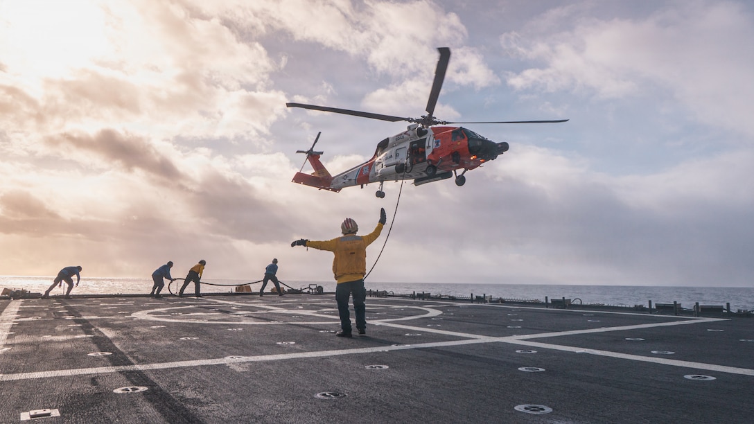 A Landing Signals Officer aboard USCGC Kimball (WMSL 756) directs a Cold Bay-based MH-60 helicopter during helicopter in-flight refueling operations in the Bering Sea, Oct. 31, 2025. The hook-up crew stood by to attach the fuel hose, a capability that allows the aircraft to remain airborne during refueling to support a sustained operational tempo and mission readiness. (U.S. Coast Guard photo by Petty Officer 2nd Class Peter Holtzhausen)