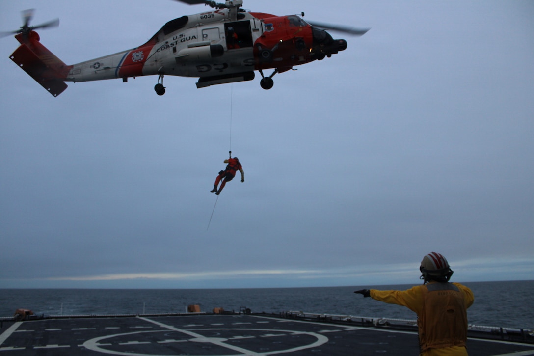 A Landing Signals Officer aboard USCGC Kimball (WMSL 756) directs an Air Station Kodiak MH-60 helicopter during hoist operations for a search and rescue exercise in the Bering Sea, Dec. 1, 2025. The evolution was designed to enhance air-surface coordination and improve readiness to respond to maritime emergencies. (U.S. Coast Guard photo by Petty Officer 2nd Class Emigdio Virgen)