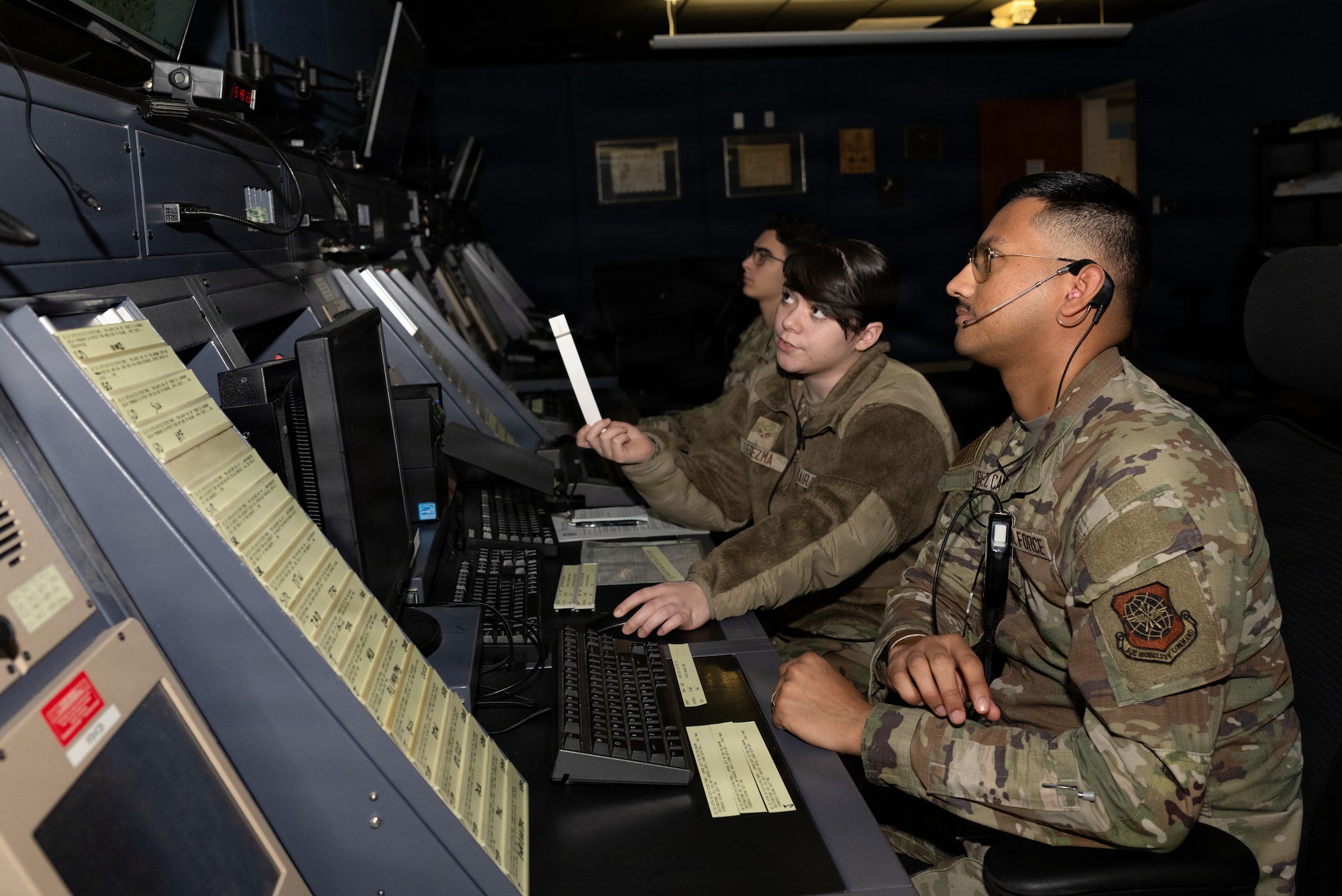 U.S. Air Force Senior Airman Alora-Jade Ledezma, Air Traffic Control Radar Approach Control trainer, demonstrates proper procedures for Airman 1st Class Juan Lopez Campos, ATC RAPCON apprentice, at Dover Air Force Base, Delaware, Dec. 29, 2025. The RAPCON is a facility that provides guidance and communication in the airspace from 2,500 feet above ground level up to an altitude of 7,000 feet in the air.