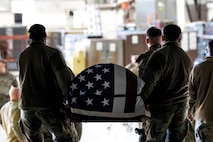 A photo of honor guardsmen carrying a casket out of a C-17 Globemaster III.