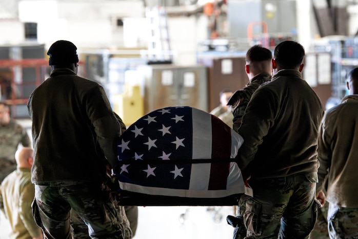 A photo of honor guardsmen carrying a casket out of a C-17 Globemaster III.