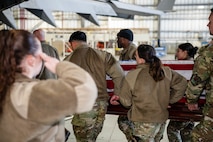 A photo of a group of Airmen carrying a casket while being saluted.