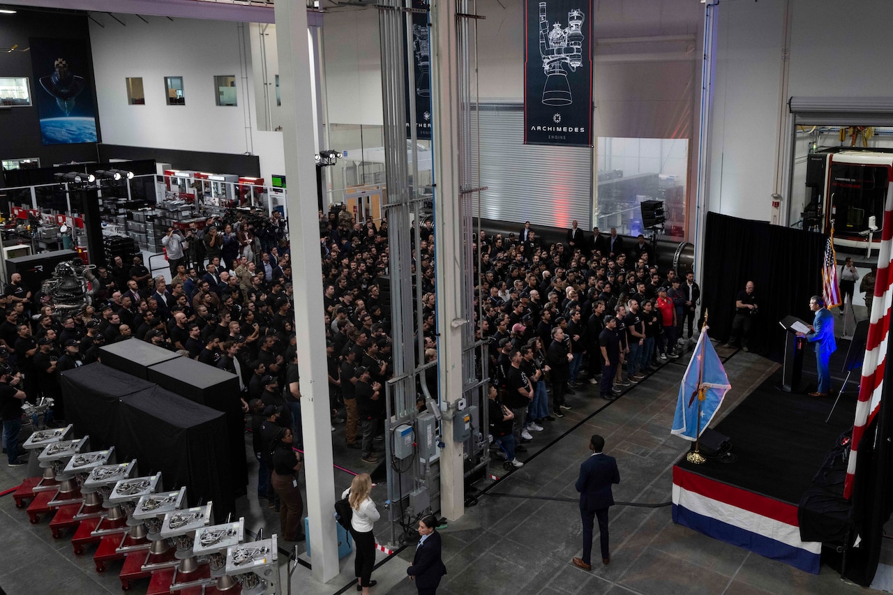 An audience sits in front of a stage with flags.
