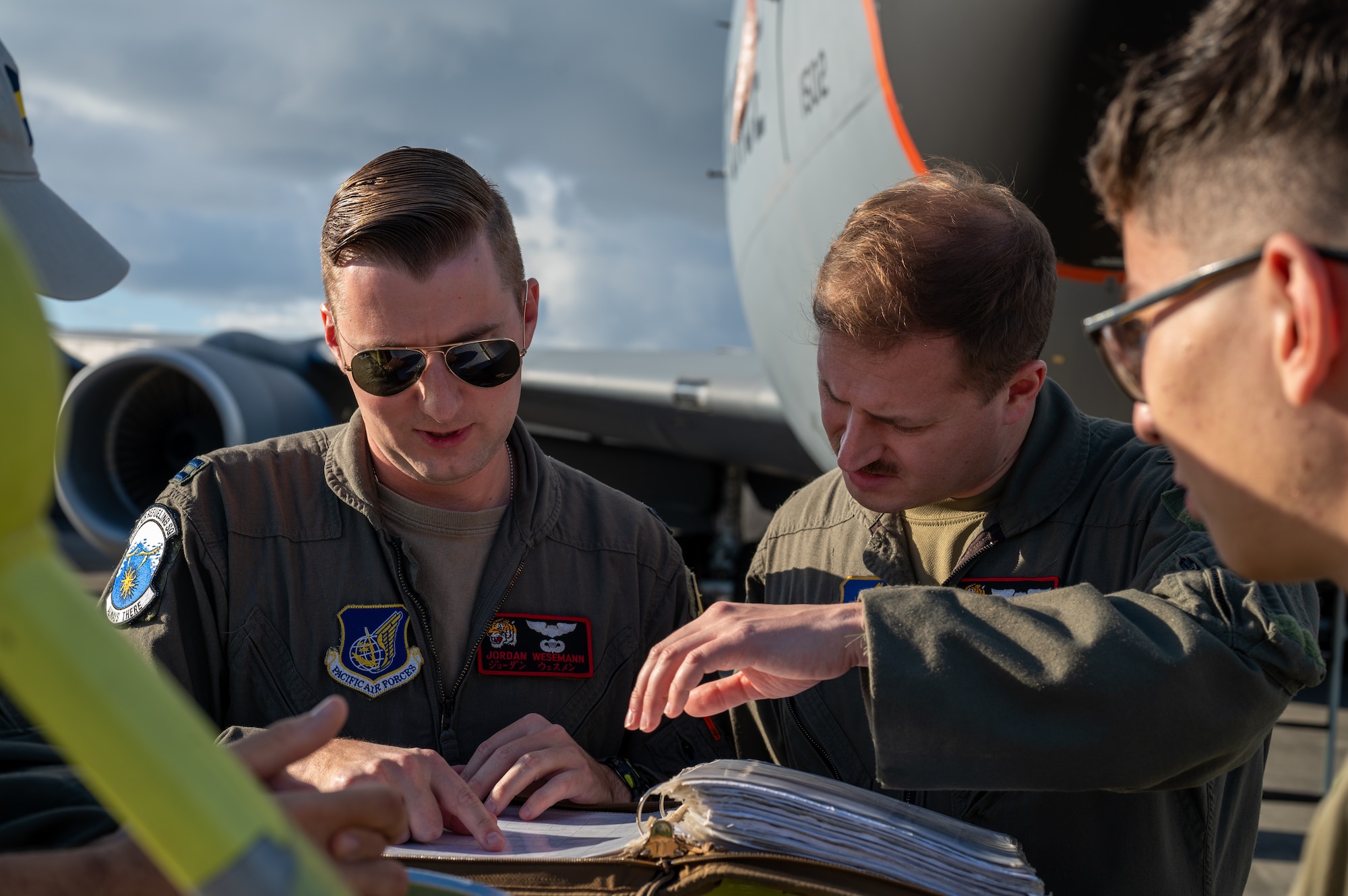 two pilots look at a binder with paper infront of a KC0-135