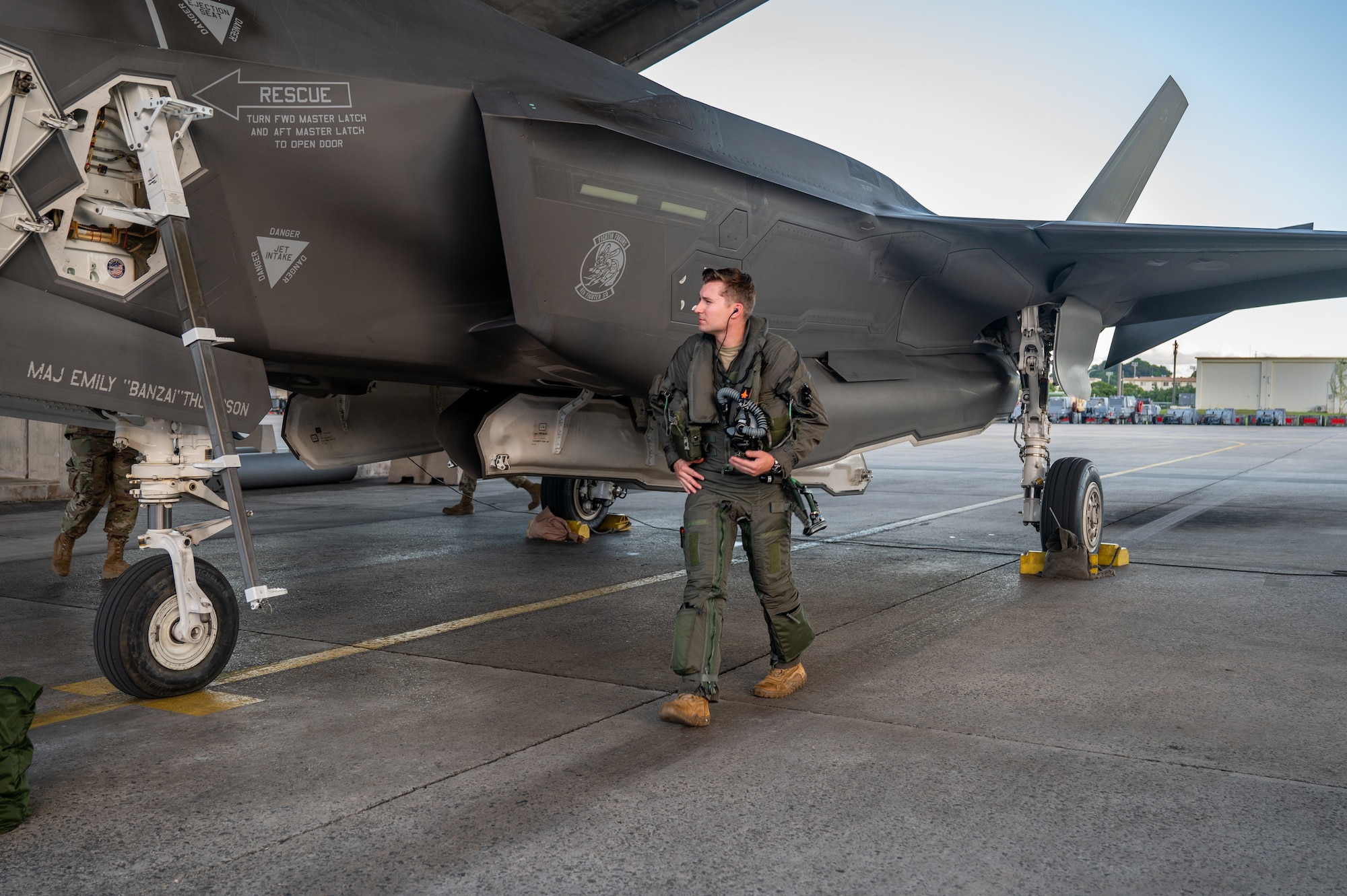 pilot in green pickle suit walks next to his fighter jet while inspecting it