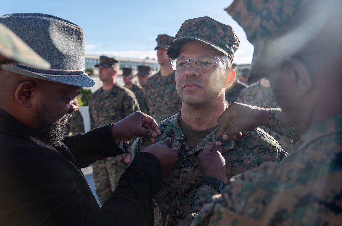 Retired U.S. Marine Corps Master Sgt. Hareko Keel, left, and Sgt. Maj. Erick Richburg, right, sergeant major of Marine Wing Headquarters Squadron 1, 1st Marine Aircraft Wing, pin the rank of first sergeant onto 1st Sgt. Christopher McCullar during McCullar’s redesignation ceremony on Camp Foster, Okinawa, Japan, Jan. 9, 2026. McCullar was selected for a lateral move to first sergeant under the new E-8 transfer pilot initiative. McCullar will take over as the senior enlisted advisor for Communications Company, 3rd Marine Littoral Regiment, 3rd Marine Division. (U.S. Marine Corps photo by Cpl. Jeremiah Barksdale)