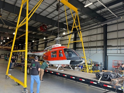 A person in civilian clothing inspects a helicopter as a second person watches.