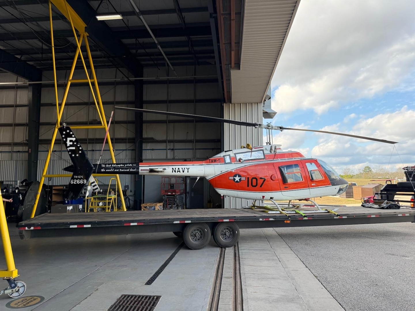 A flatbed tows a military aircraft from an airport hangar.
