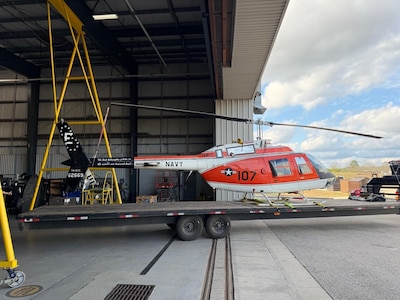 A flatbed tows a military aircraft from an airport hangar.