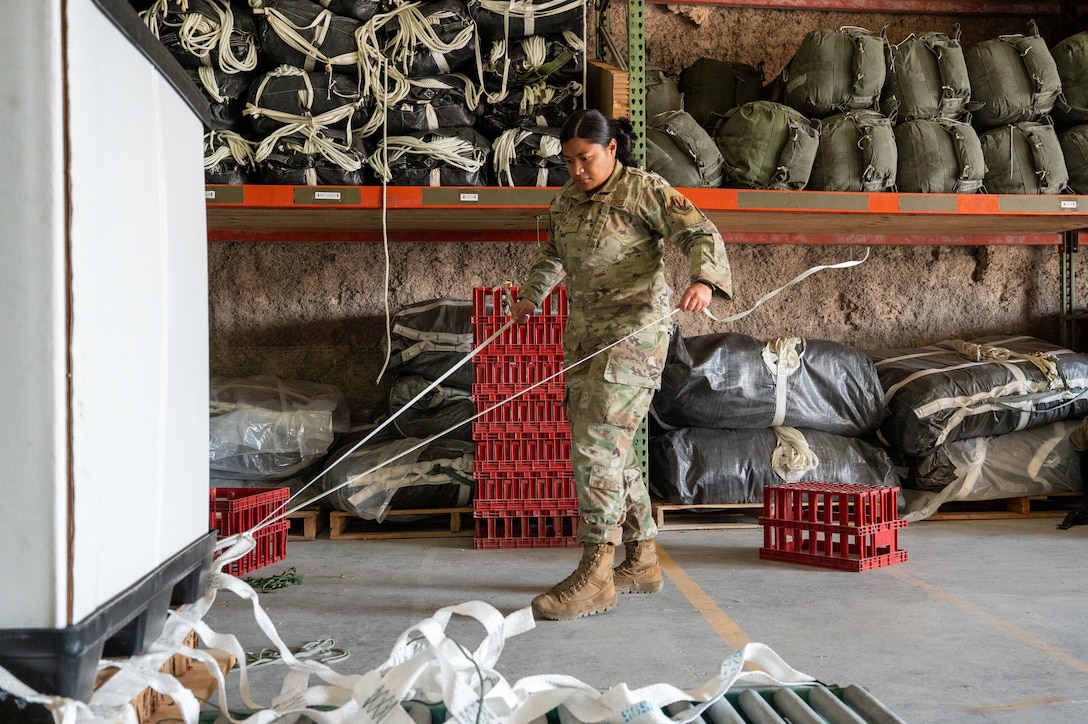 U.S. Air Force Senior Airman Mavaeao Tili, 26th Expeditionary Rescue Squadron aircrew flight equipment technician, unravels cord during an Army rigger training course in the U.S. Central Command area of responsibility, Dec. 19, 2025. Twelve Airmen from across the AOR participated in the five-day course, which covered rigging low-cost high velocity and low-cost low-velocity parachutes onto container delivery systems. (U.S. Air Force photo by Tech. Sgt. Kristen Pittman)