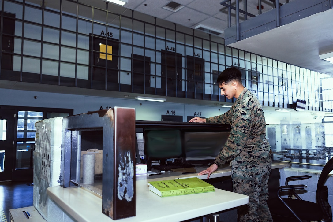 U.S. Marine Corps Cpl. Jonathan Diaz, facilities escort, Marine Corps Installations East-Marine Corps Base (MCB) Camp Lejeune Regional Brig, stands at the brig duty table on MCB Camp Lejeune, Dec. 15, 2025. There are four platoons of Marines in the brig, rotating between day and night shifts every three months. (U.S. Marine Corps photo by Cpl. Loriann Dauscher) (This photo has been blurred to obstruct view of sensitive information.)