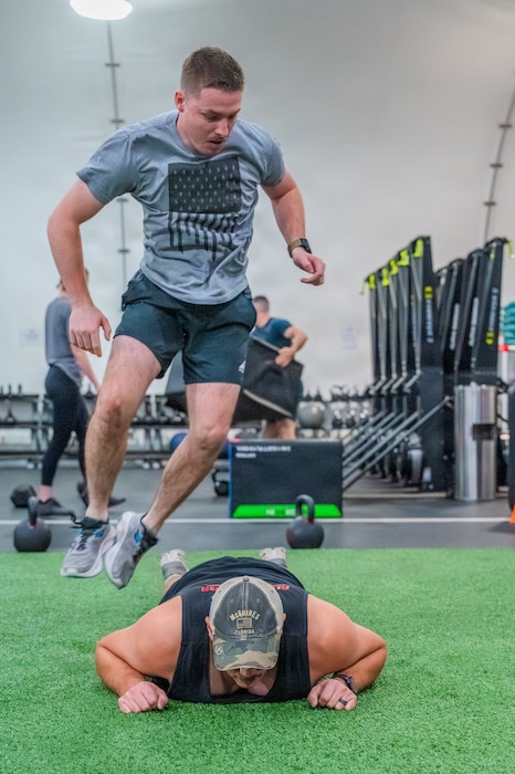 U.S. Air Force Airman 1st Class Alec Foster (left), 56th Civil Engineer Squadron explosive ordnance disposal technician, jumps over Senior Airman James Little (center), 56th Civil Engineer Squadron EOD technician, during an annual memorial workout, Dec. 19, 2025, at Luke Air Force Base, Arizona.