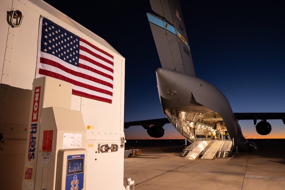 Foreground left is a container on right is a plane with an open cargo door