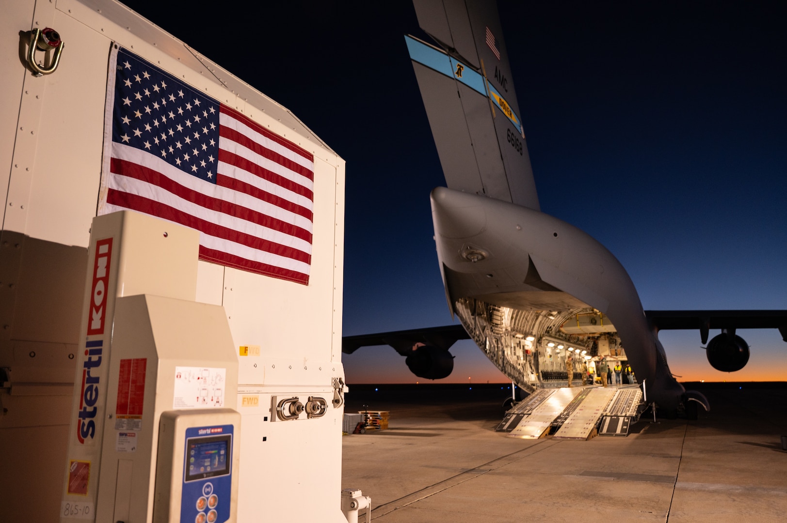 Foreground left is a container on right is a plane with an open cargo door