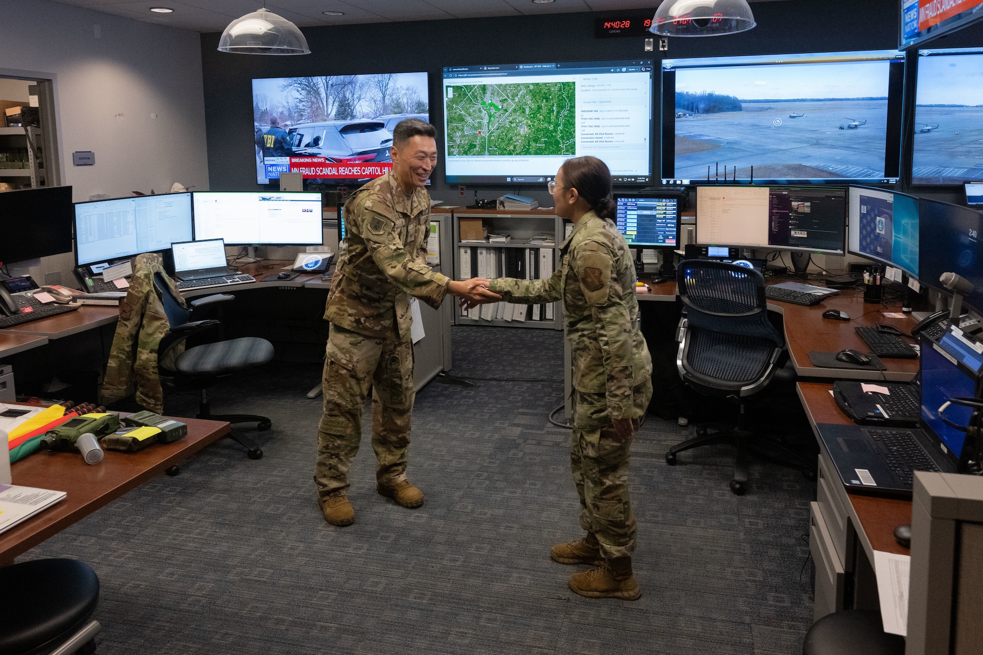 Man and woman shake hands in a room with multiple screens.
