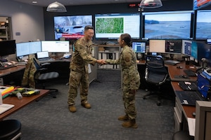 Man and woman shake hands in a room with multiple screens.