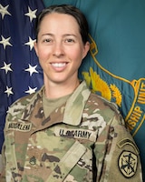 Woman in U.S. Army uniform standing in front of two flags.