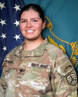 Woman in U.S. Army uniform standing in front of two flags.