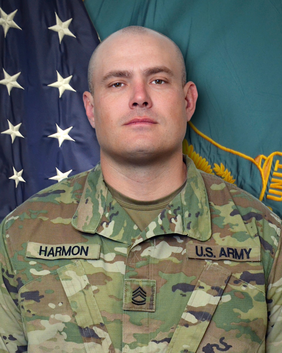 Man in U.S. Army uniform standing in front of two flags.