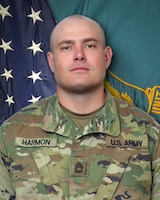 Man in U.S. Army uniform standing in front of two flags.