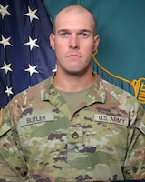 Man in U.S. Army uniform standing in front of two flags.