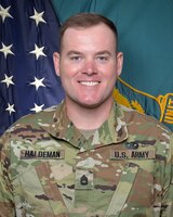 Man in U.S. Army uniform standing in front of two flags.