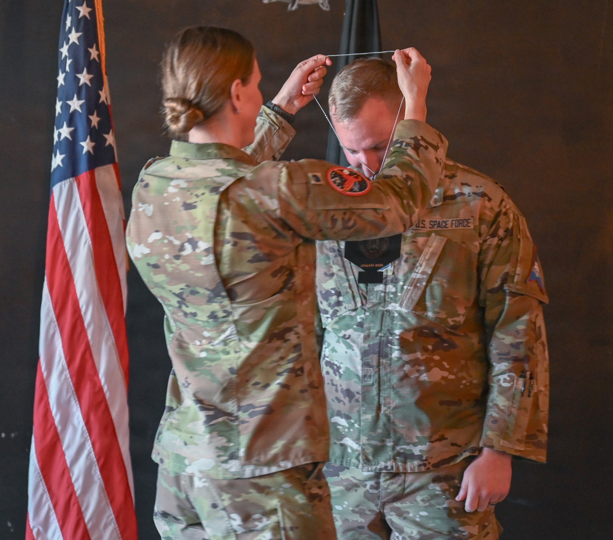 Woman places promotion medallion around the neck of Senior Master Sgt. Select Obed Hassell, Space Forces - Space Space Delta 5 senior enlisted leader, during the Senior Master Sergeant Release Party held at Vandenberg Space Force Base, Calif., Jan. 9, 2025.