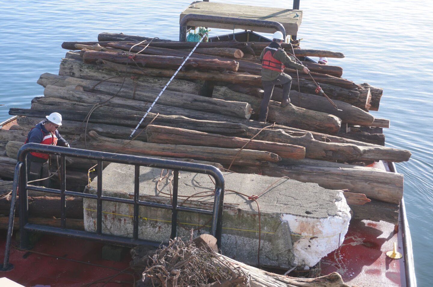 Motor Vessel (MV) Puget crew members stack recovered timber piles, for safe transportation to Lake Washington Ship Canal and Hiram M. Chittenden Locks, Seattle.  The vessel patrols the inland waters of Puget Sound, collecting debris and obstructions to navigation.