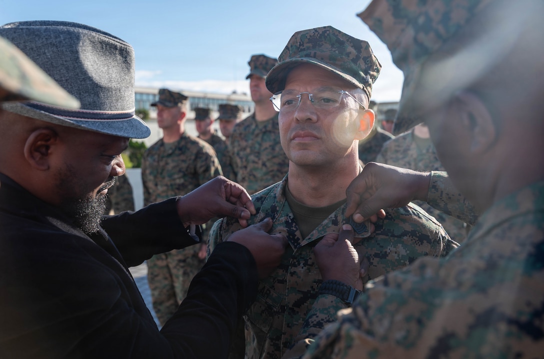 Retired U.S. Marine Corps Master Sgt. Hareko Keel, left, and Sgt. Maj. Erick Richburg, right, sergeant major of Marine Wing Headquarters Squadron 1, 1st Marine Aircraft Wing, pin the rank of first sergeant onto 1st Sgt. Christopher McCullar during McCullar’s redesignation ceremony on Camp Foster, Okinawa, Japan, Jan. 9, 2026. McCullar was selected for a lateral move to first sergeant under the new E-8 transfer pilot initiative. McCullar will take over as the senior enlisted advisor for Communications Company, 3rd Marine Littoral Regiment, 3rd Marine Division. (U.S. Marine Corps photo by Cpl. Jeremiah Barksdale)