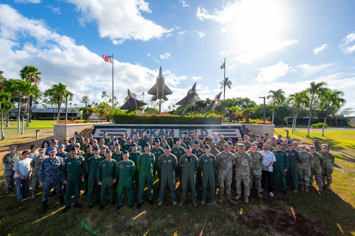 Allied air operations leaders from the United States, Japan and Australia pose for a group photo in front of the Missing Man Formation at Joint Base Pearl Harbor-Hickam, Hawaii. The formation shows four statues of jets taking off, with one going higher than the others, representing the missing man formation performed in real life.